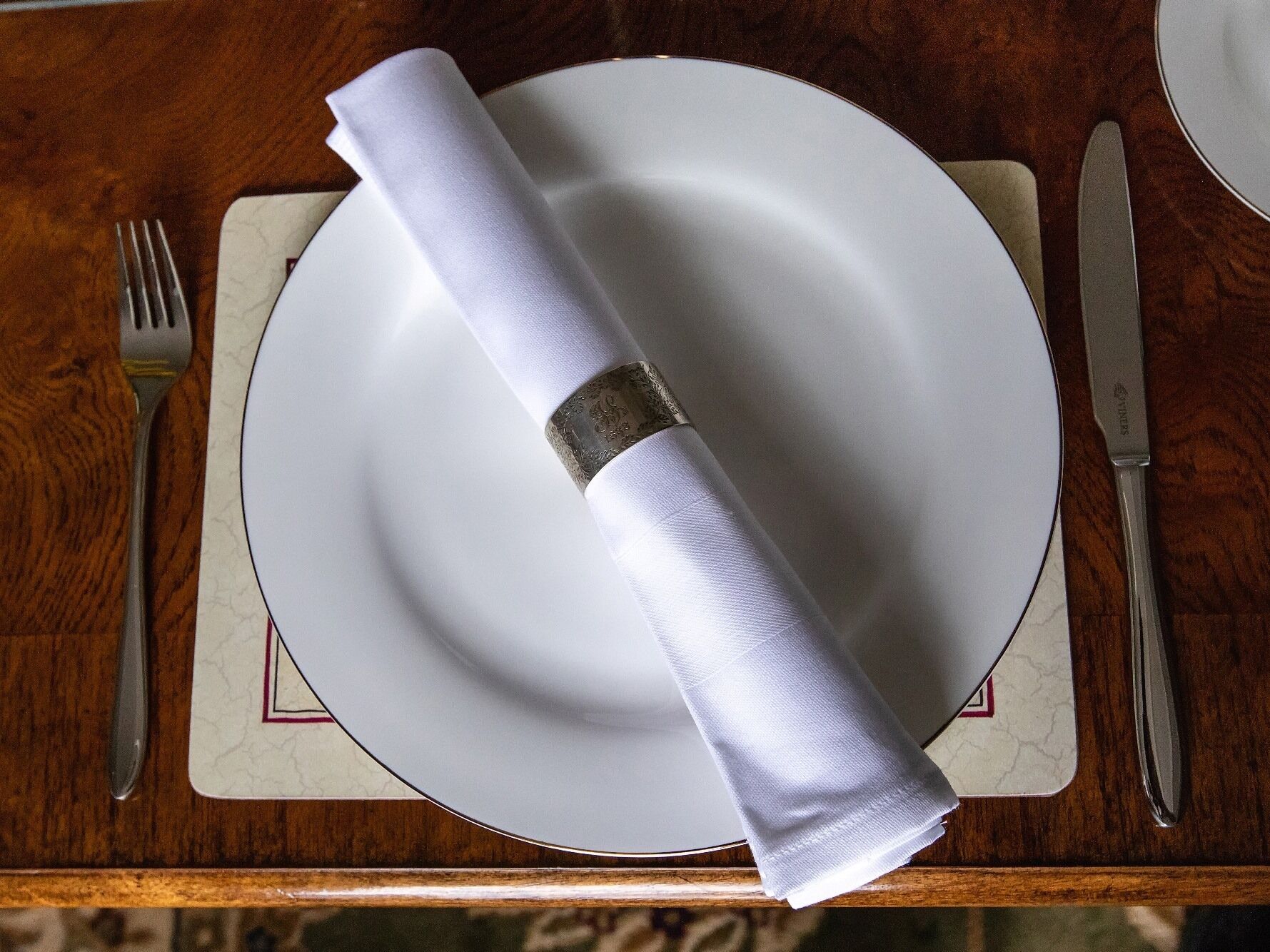 A neatly set dining table with a white plate, folded napkin, and silverware on a wooden table.