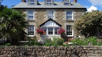 Traditional stone house with a central entrance, pitched roof, and lush greenery.