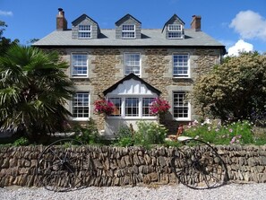 A stone house with a gabled roof, multiple windows, and a front porch with flower pots. - Pengelly Farmhouse B&B (Truro)