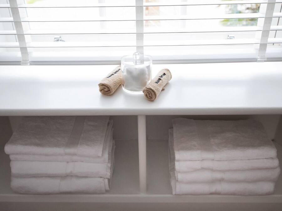 Ein Badezimmer mit Fenster, einem Glas und ordentlich zusammengelegten Handtüchern auf einem Regal.