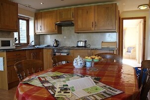 Una cocina con armarios de madera, microondas, tetera, tostadora y una mesa de comedor con un mantel individual.