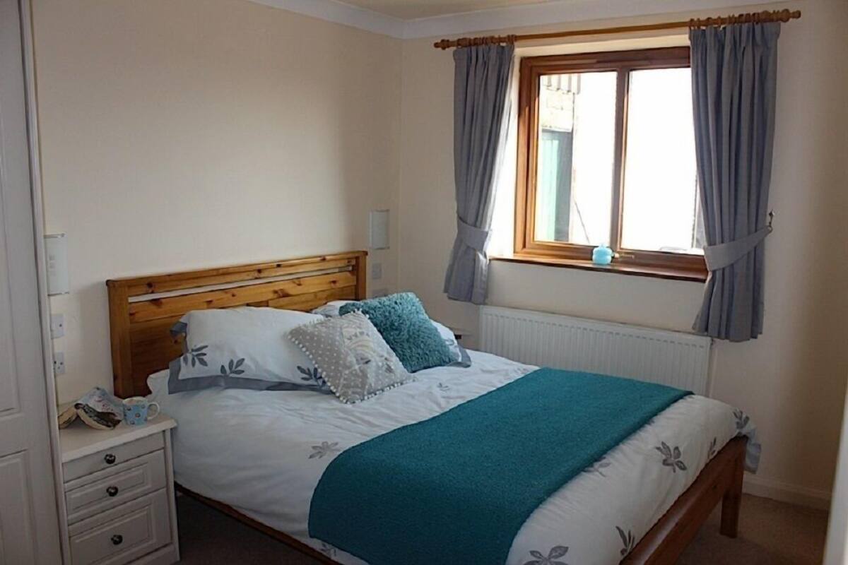 A bedroom with a wooden bed, white bedding, a teal throw blanket, and a window with curtains.
