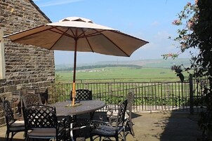 Un patio con una mesa redonda y sillas, una sombrilla y vistas a un paisaje verde.