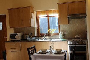Una cocina con armarios de madera, microondas, lavamanos y una mesa de comedor preparada para dos.