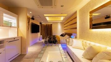 A modern hotel room with a glass coffee table, a white sofa, a flat-screen TV, and a large mirror.
