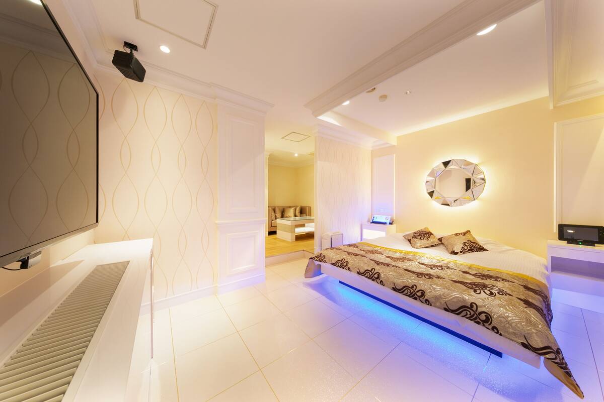 A modern bedroom with a large bed, a TV, and a bathroom visible in the background.
