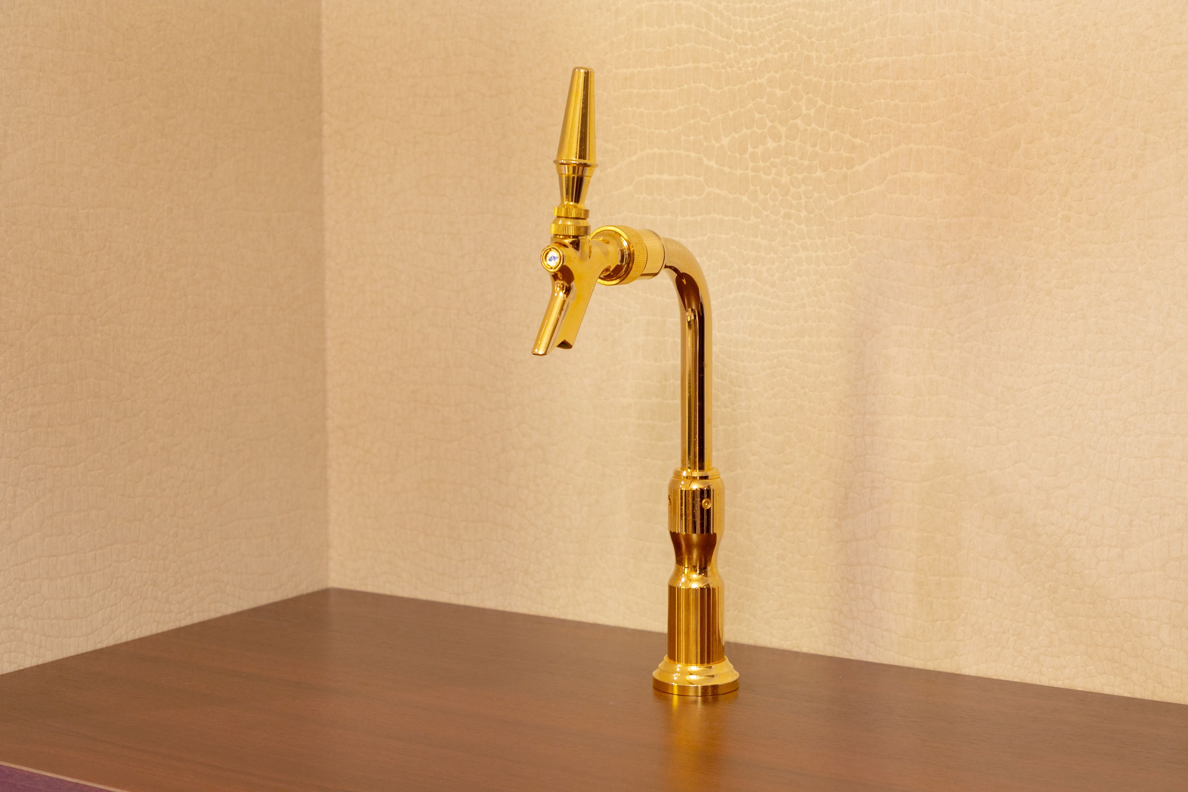 A gold-colored tap on a wooden surface against a textured wall.