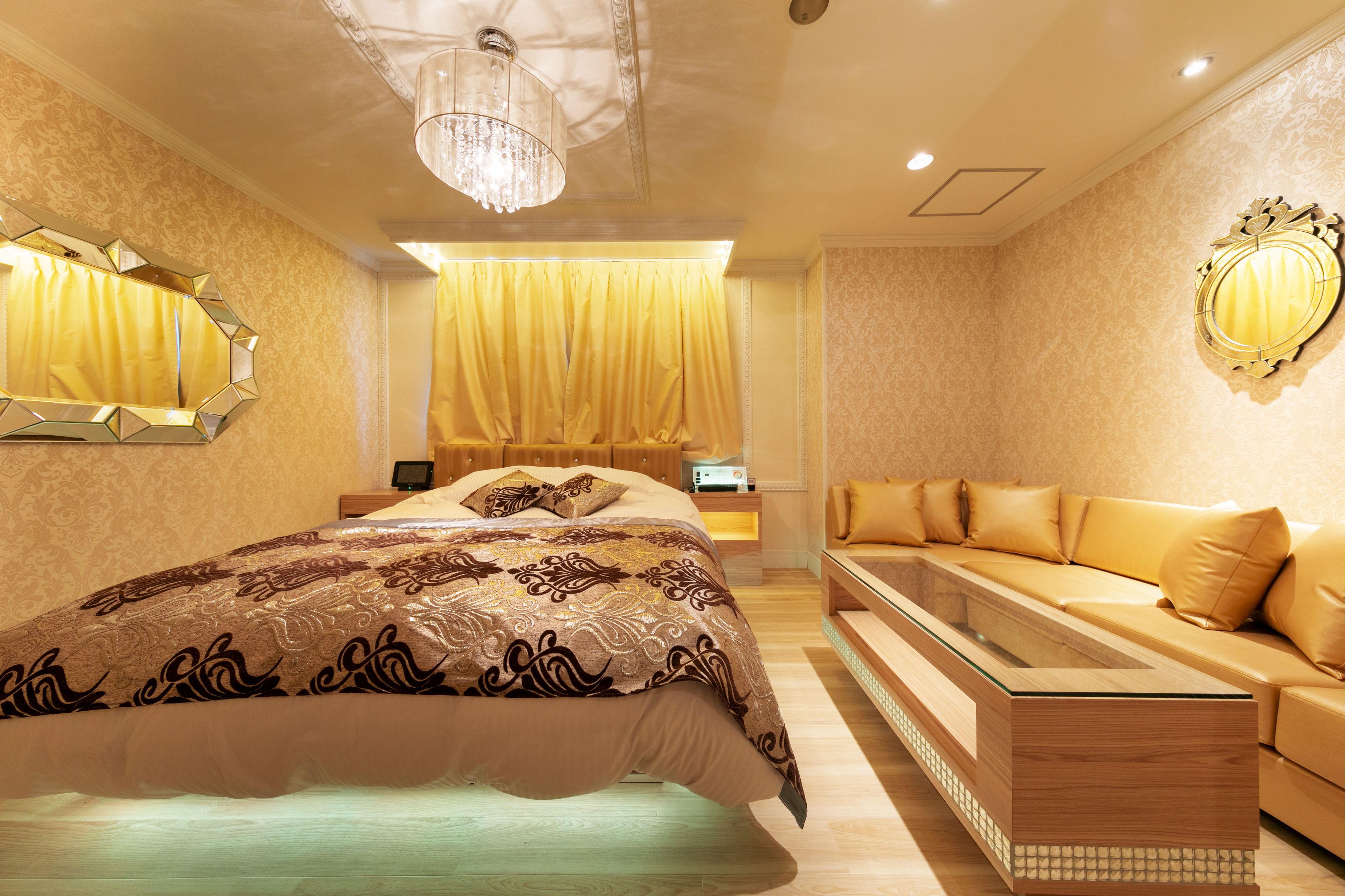A modern bedroom with a large bed, a glass-top coffee table, a sofa, and a decorative mirror.