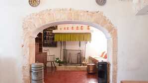A rustic room with a stone archway, a green curtain, a wooden chair, a small table, and a metal barrel. - Masseria Murgia Albanese (Noci)