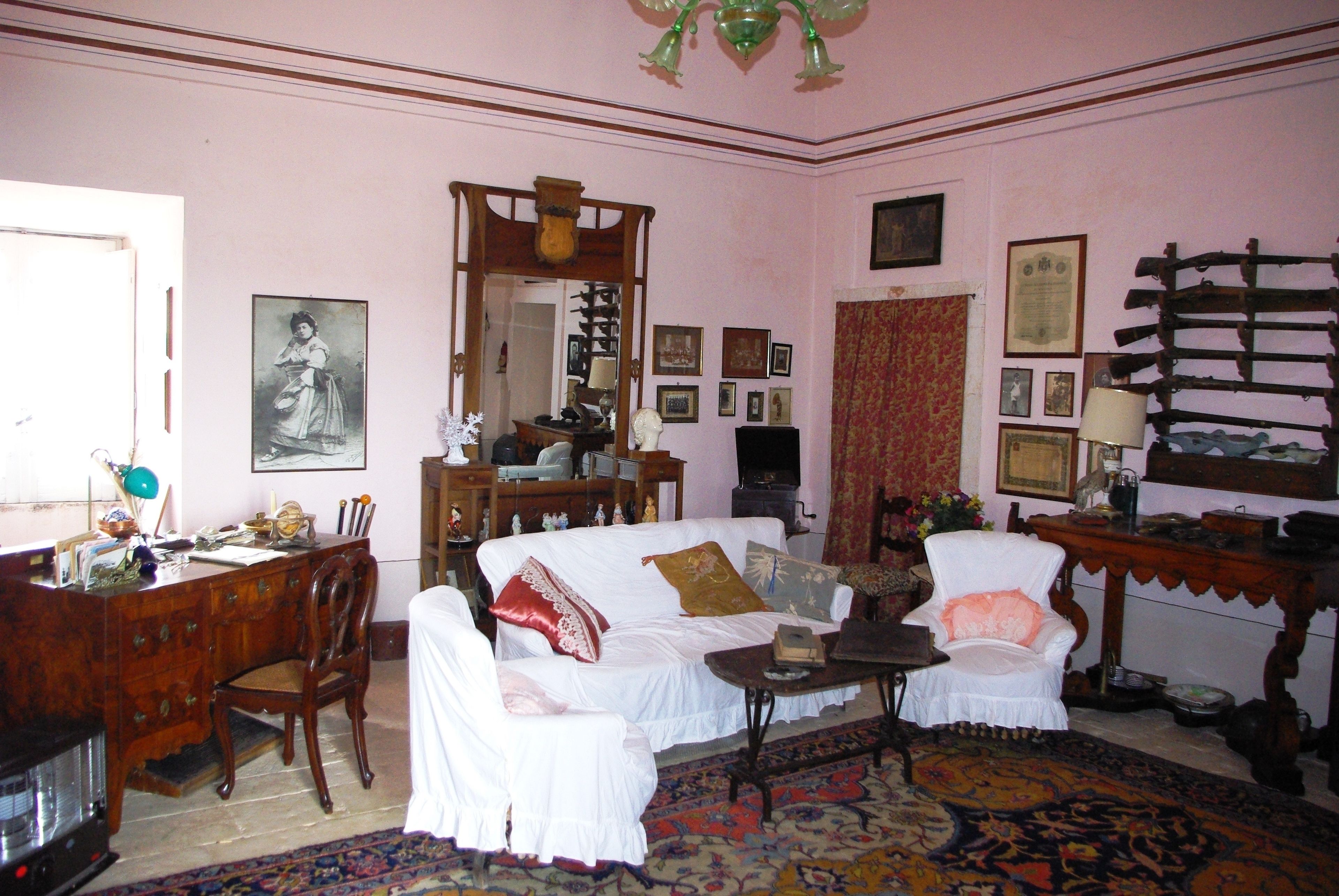 Una habitación con un sofá blanco, un escritorio de madera, una silla, un espejo y varias imágenes enmarcadas en las paredes.