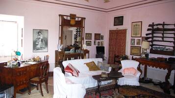 Una habitación con un sofá blanco, un escritorio de madera, una silla, un espejo y varias imágenes enmarcadas en las paredes.