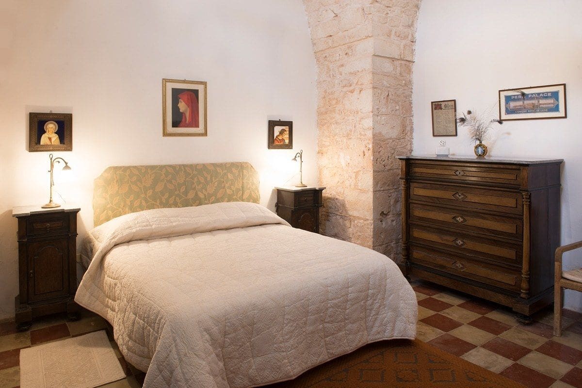 Une chambre à coucher avec un lit, des tables de chevet, une commode et un mur en pierre.