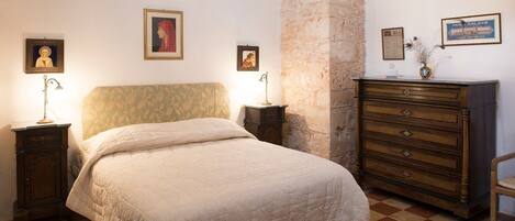 A bedroom with a bed, nightstands, a dresser, and a stone wall.