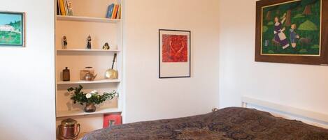 A bedroom with a large bed, a bookshelf, and a painting on the wall.