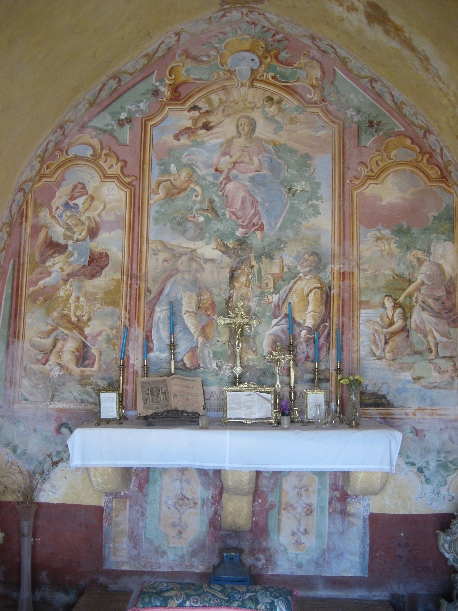 An ornate chapel interior with a religious mural, a white altar, and candles.