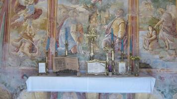 An ornate chapel interior with a religious mural, a white altar, and candles.