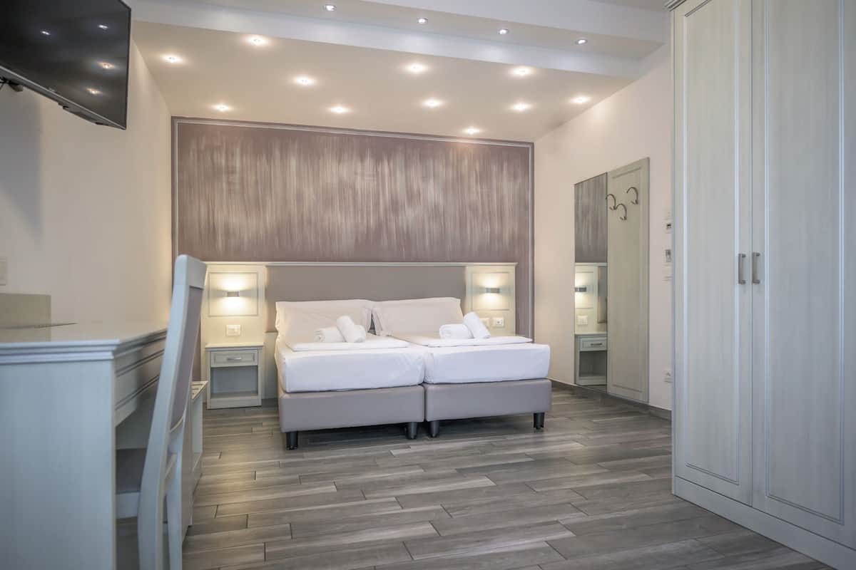 A modern bedroom with a large bed, bedside lamps, a TV, and a wardrobe.