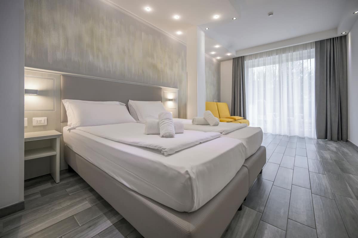 A modern hotel room with a large bed, bedside tables, a chair, and a large window with curtains.