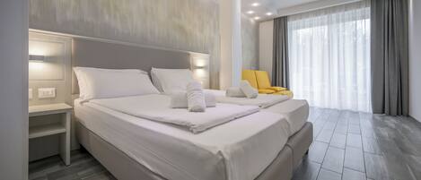 Een moderne hotelkamer met een groot bed, nachtkastjes, een stoel en een groot raam met gordijnen.
