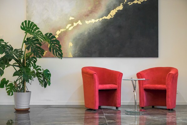 Un interior moderno con dos sillones rojos, una planta de monstera en maceta y un cuadro abstracto grande en la pared.