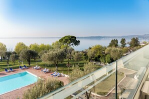 A pool with lounge chairs, a clear view of the sea, and a grassy area with trees. - Hotel Villa Paradiso Suite  (Moniga del Garda)
