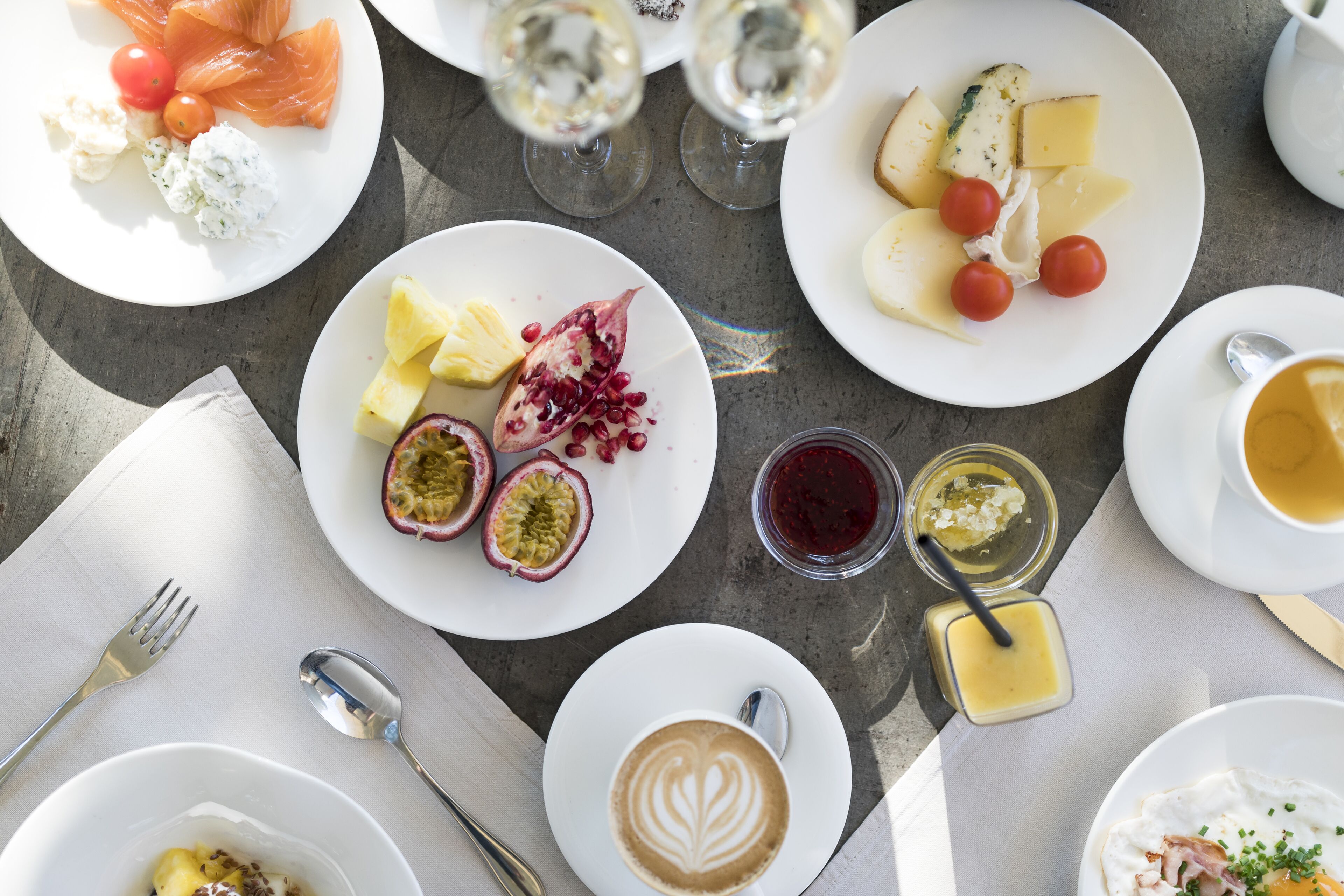 Una mesa con varios platos de comida, incluyendo salmón, queso y frutas, además de vasos de bebidas.