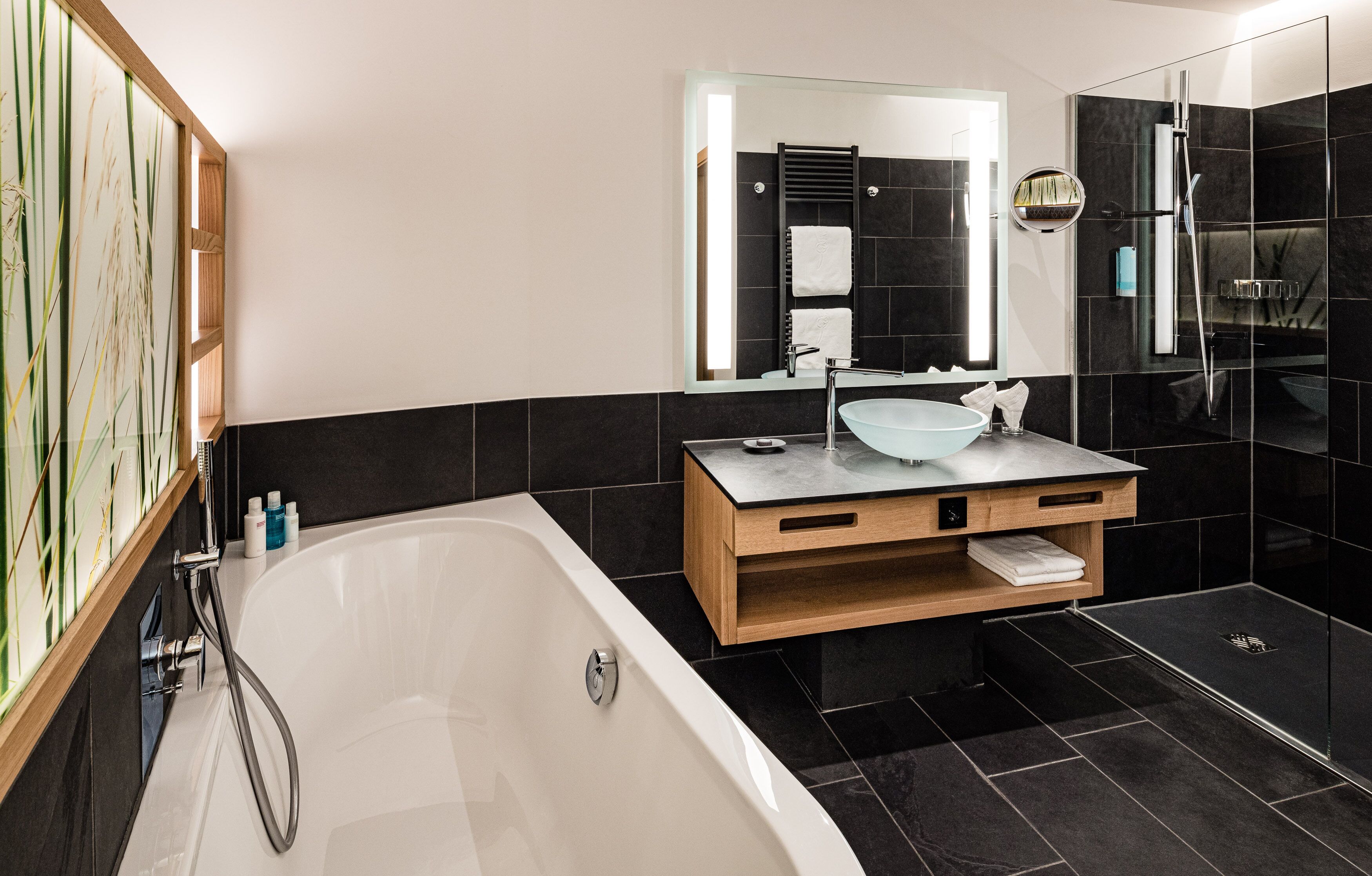 Ein modernes Badezimmer mit freistehender Badewanne, einem Holzwaschtisch mit Glaskonsole und einem großen Spiegel.