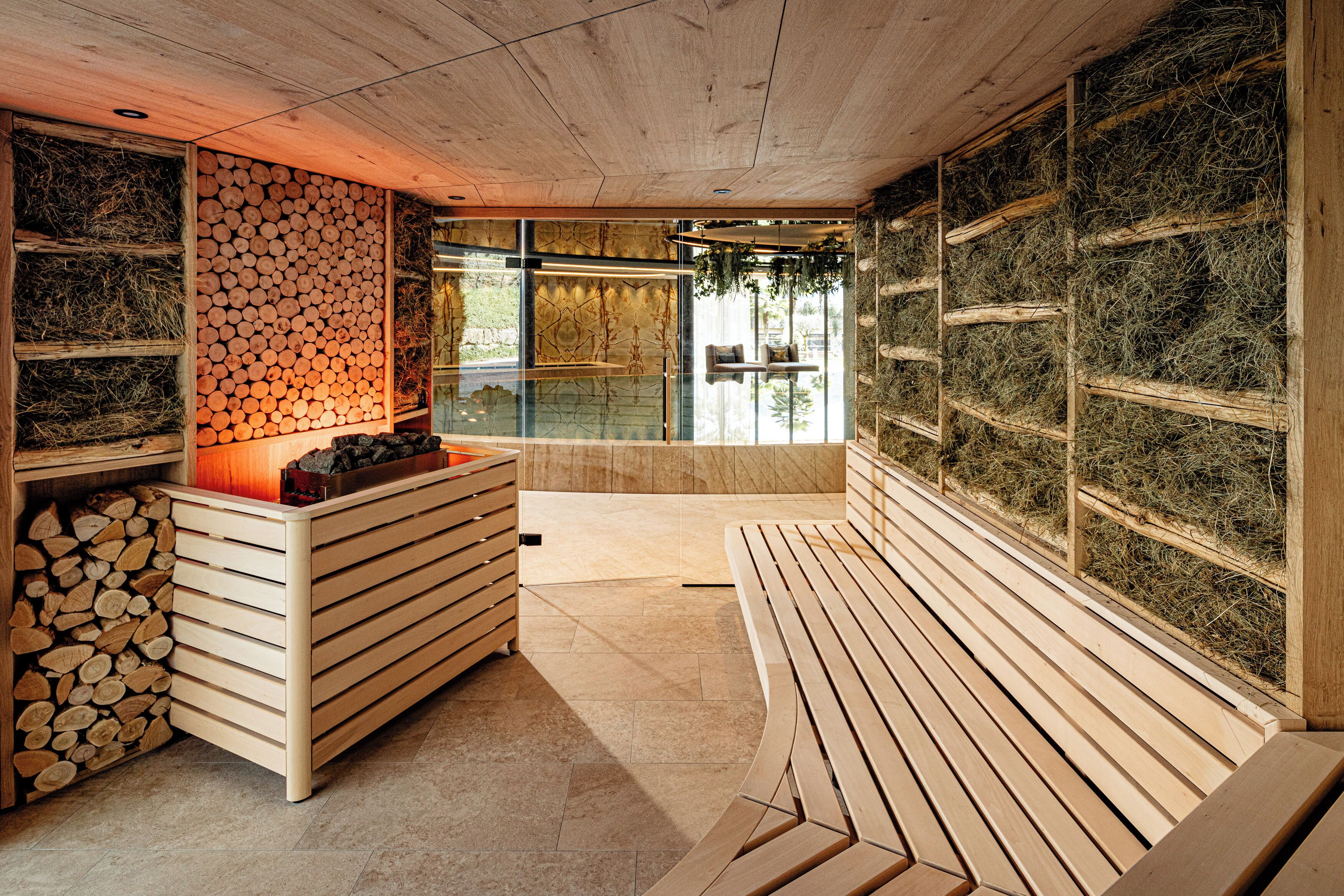 A sauna with wooden benches, a wall of stacked logs, and a glass partition.
