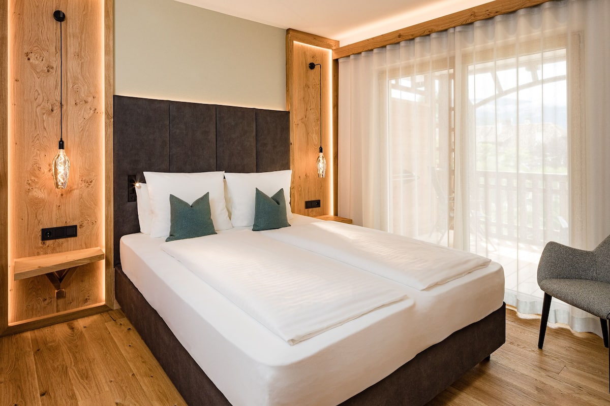 A modern hotel room with a large bed, wooden paneling, and a view of the outdoors.