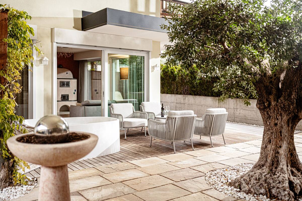 An outdoor patio with modern furniture, a large tree, and a stone birdbath.