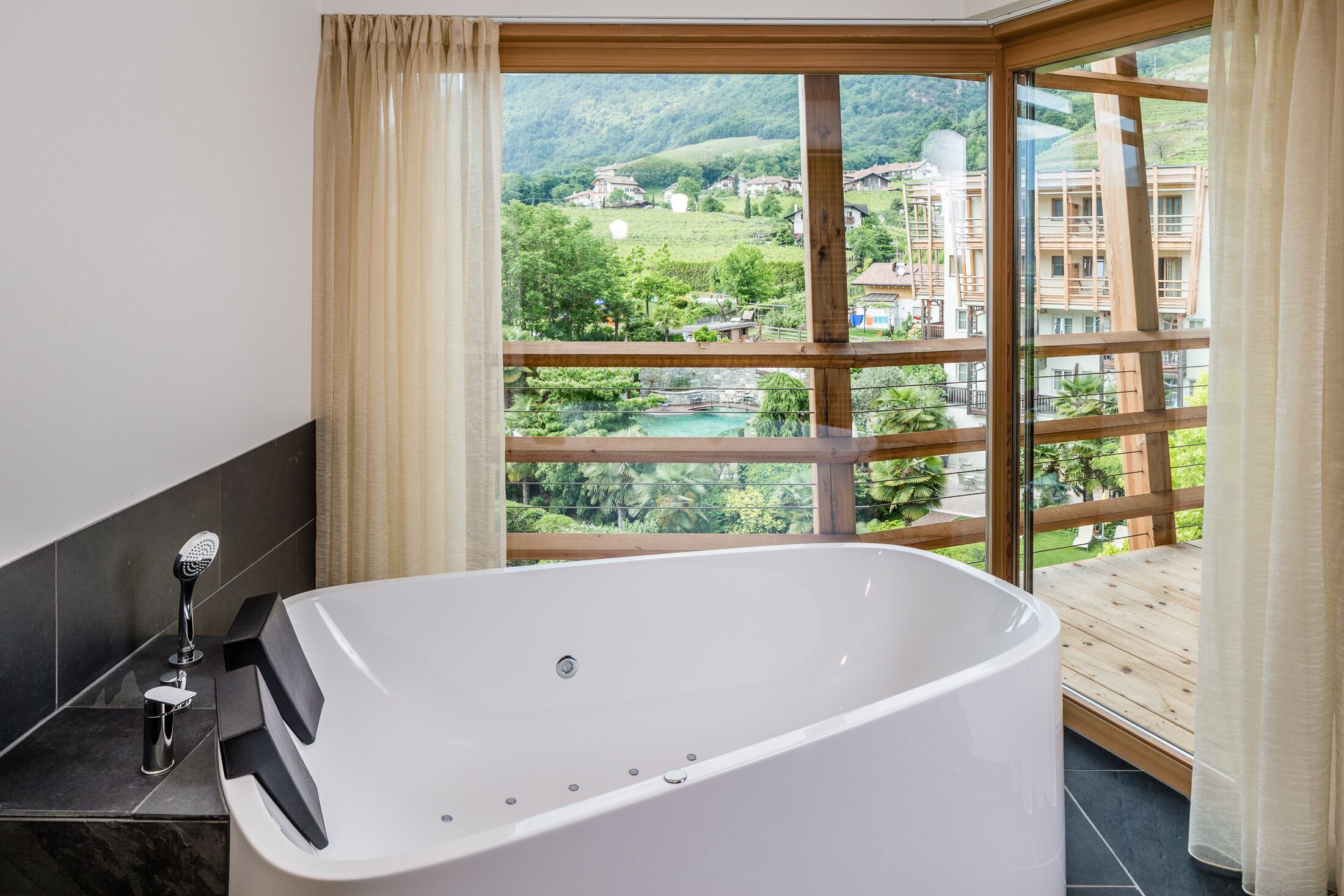 A modern bathroom with a freestanding bathtub, a shower with a handheld showerhead, and a view of a mountainous landscape through large windows.