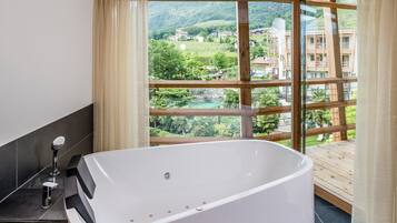 A modern bathroom with a freestanding bathtub, a shower with a handheld showerhead, and a view of a mountainous landscape through large windows.