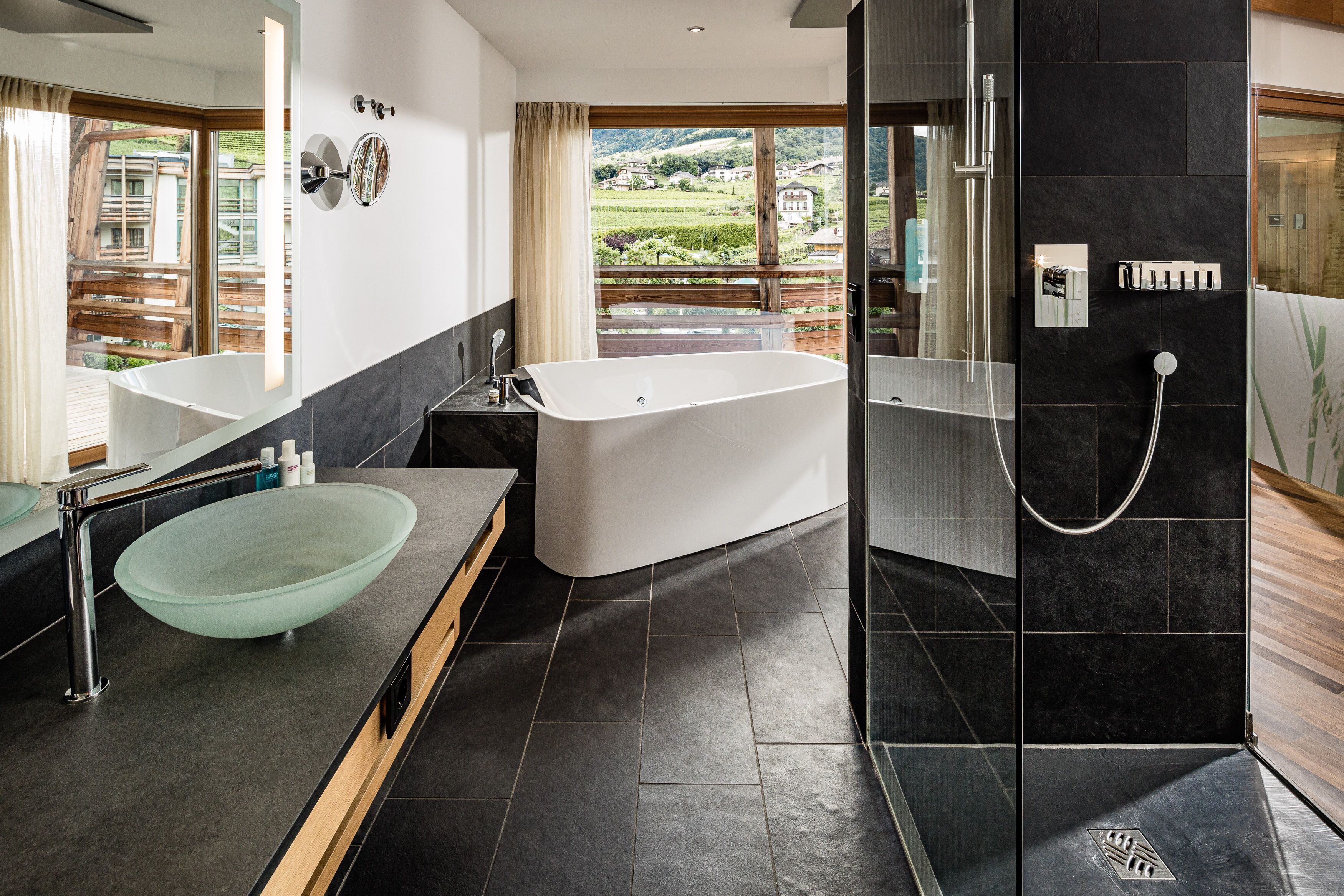A modern bathroom with a freestanding bathtub, a glass bowl sink, and a shower area.