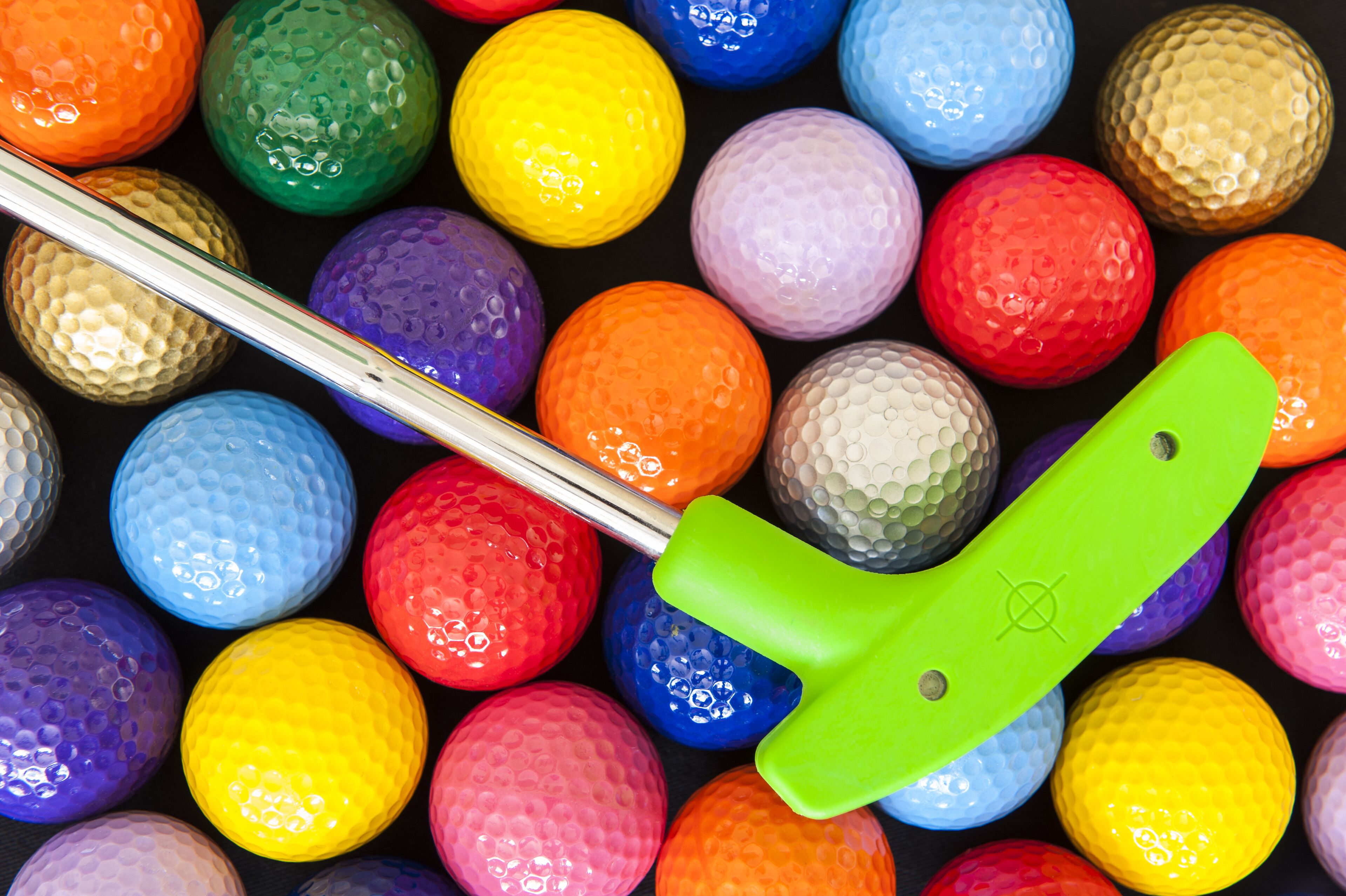Una colección de pelotas de golf en varios colores, con un palo de golf en el centro.