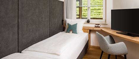 Un dormitorio con cama, escritorio, silla, televisor y ventana con vistas a zonas verdes.