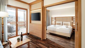 A hotel room with a bed, a TV, a wooden desk, and a balcony with outdoor furniture.
