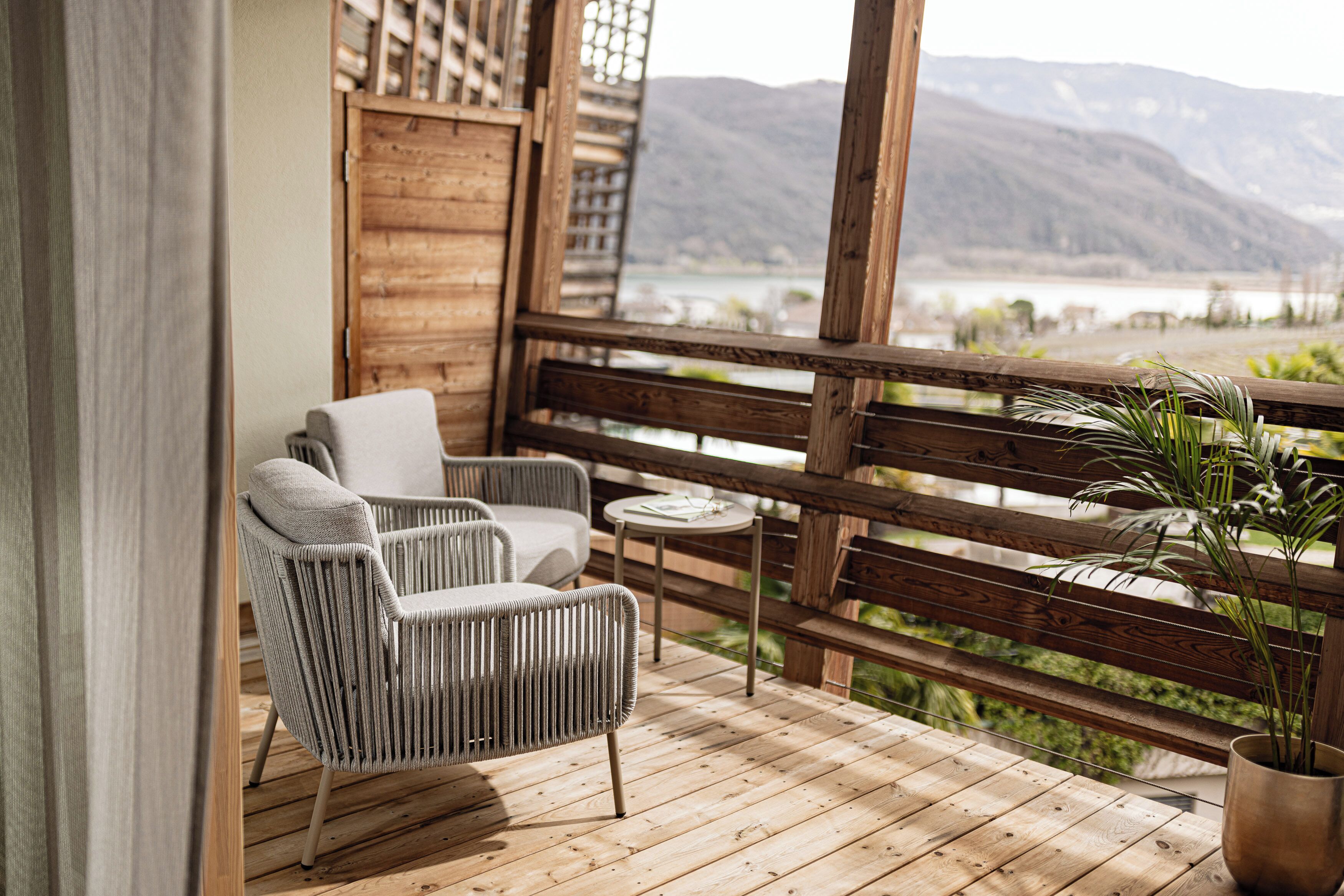 Una terraza de madera con una silla y una pequeña mesa, con vista a un lago y montañas.