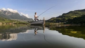 Eine Person angelt sich von einem Boot auf einem ruhigen See, im Hintergrund sind Berge zu sehen.