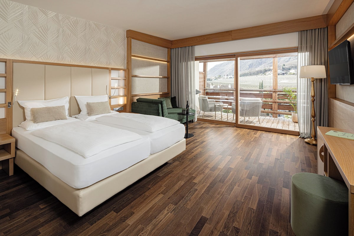 A hotel room with a large bed, a desk, a chair, and a balcony with a view of the mountains.