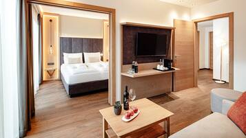 Ein modernes Hotelzimmer mit Bett, Wandfernseher, einem kleinen Tisch mit Flasche und Gläsern sowie einer Couch.
