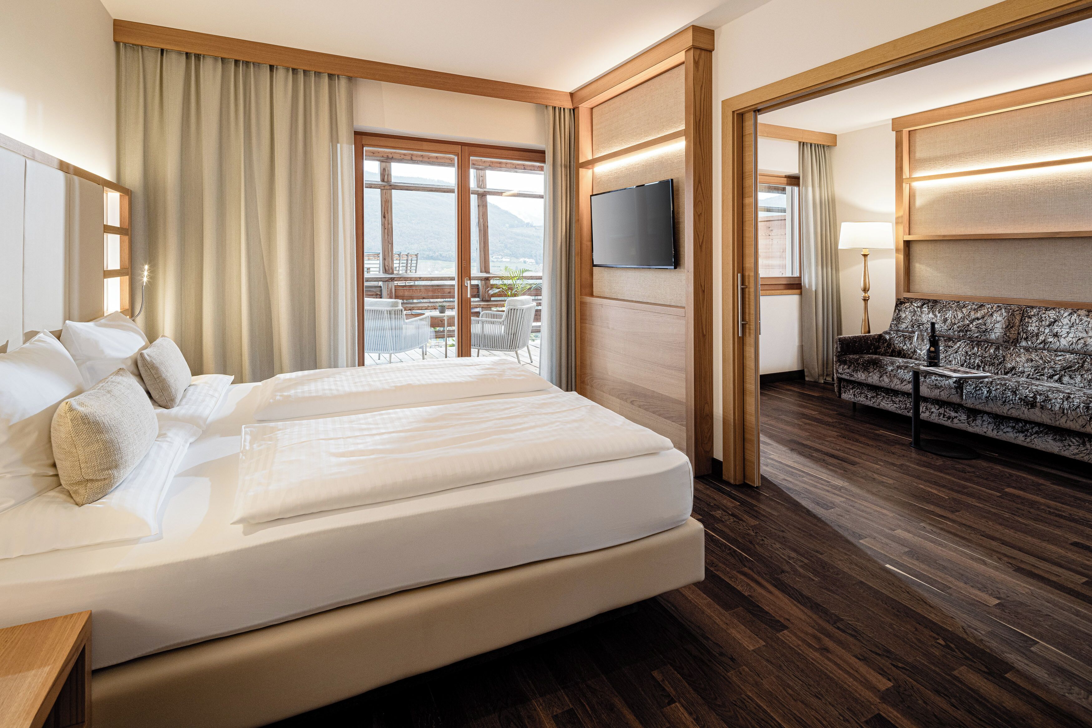 Una habitación de hotel con una cama grande, un sofá, un televisor y un balcón con vistas.