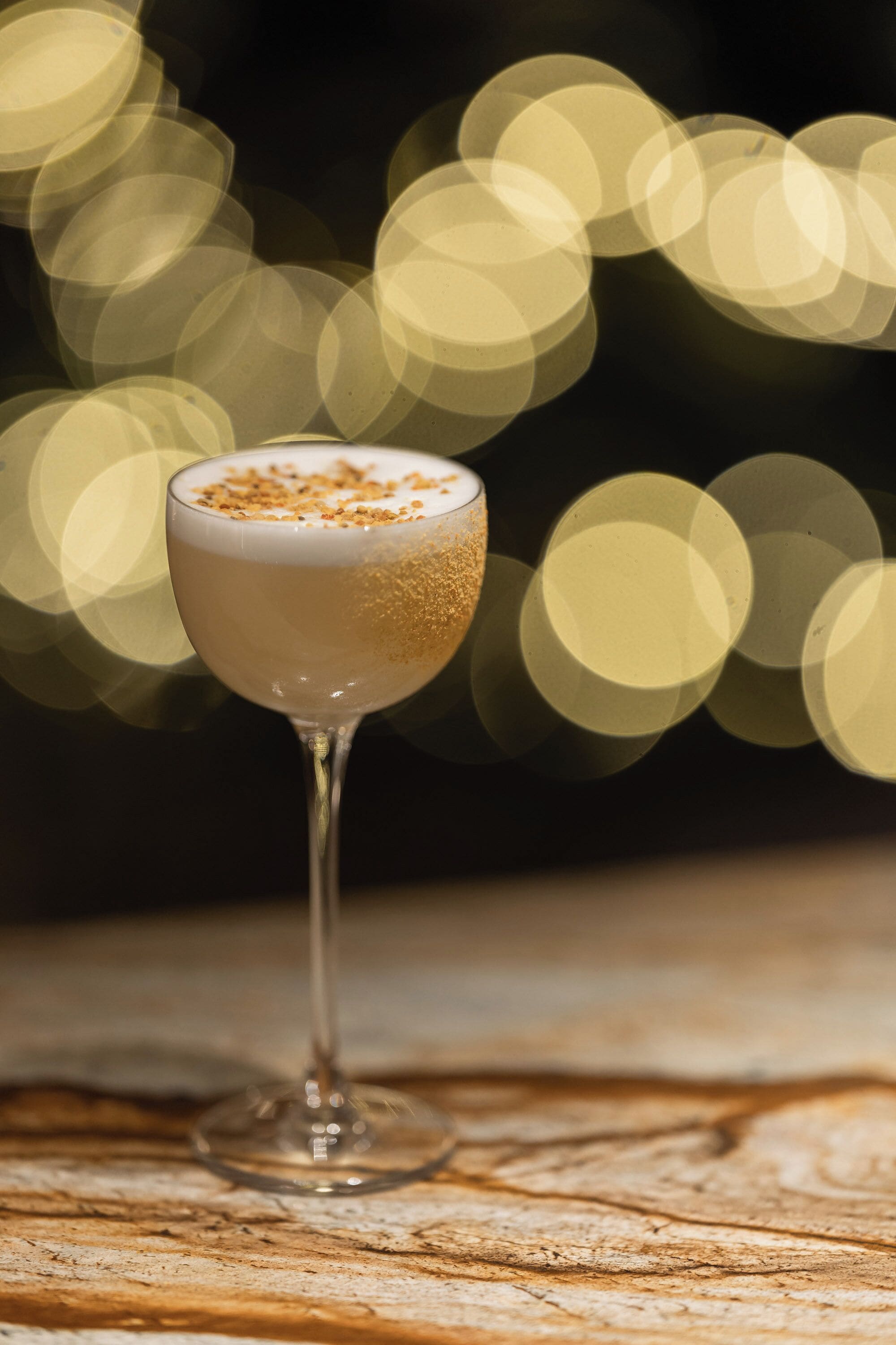 Un cocktail in un bicchiere con una schiuma in cima, posato su un piano di legno.