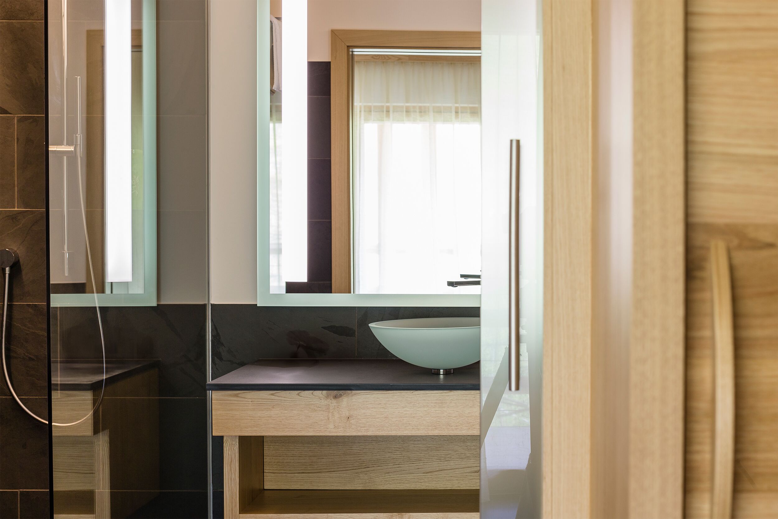 A modern bathroom with a large mirror, a wooden vanity, and a glass shower enclosure.