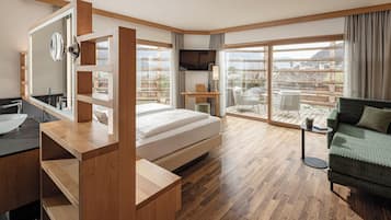 Una habitación de hotel moderna con piso de madera, una cama, un escritorio, un televisor, un balcón con vistas y un sofá verde.