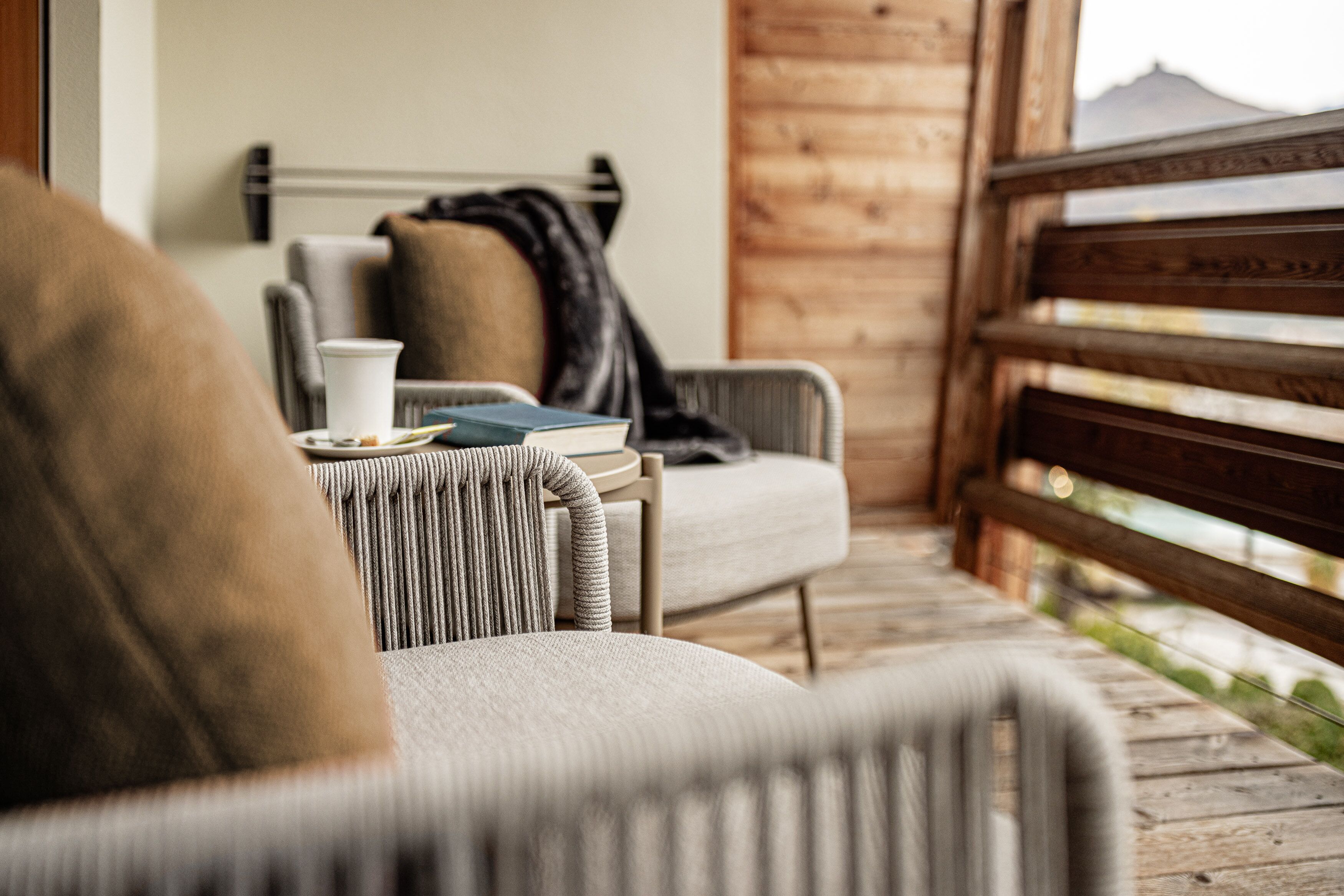 Een gezellige zithoek met een comfortabele fauteuil, een klein tafeltje met een kopje en boek, en een houten leuning.