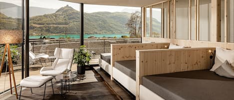 A modern room with a bed, a seating area with a view of a lake and mountains, and a large window.