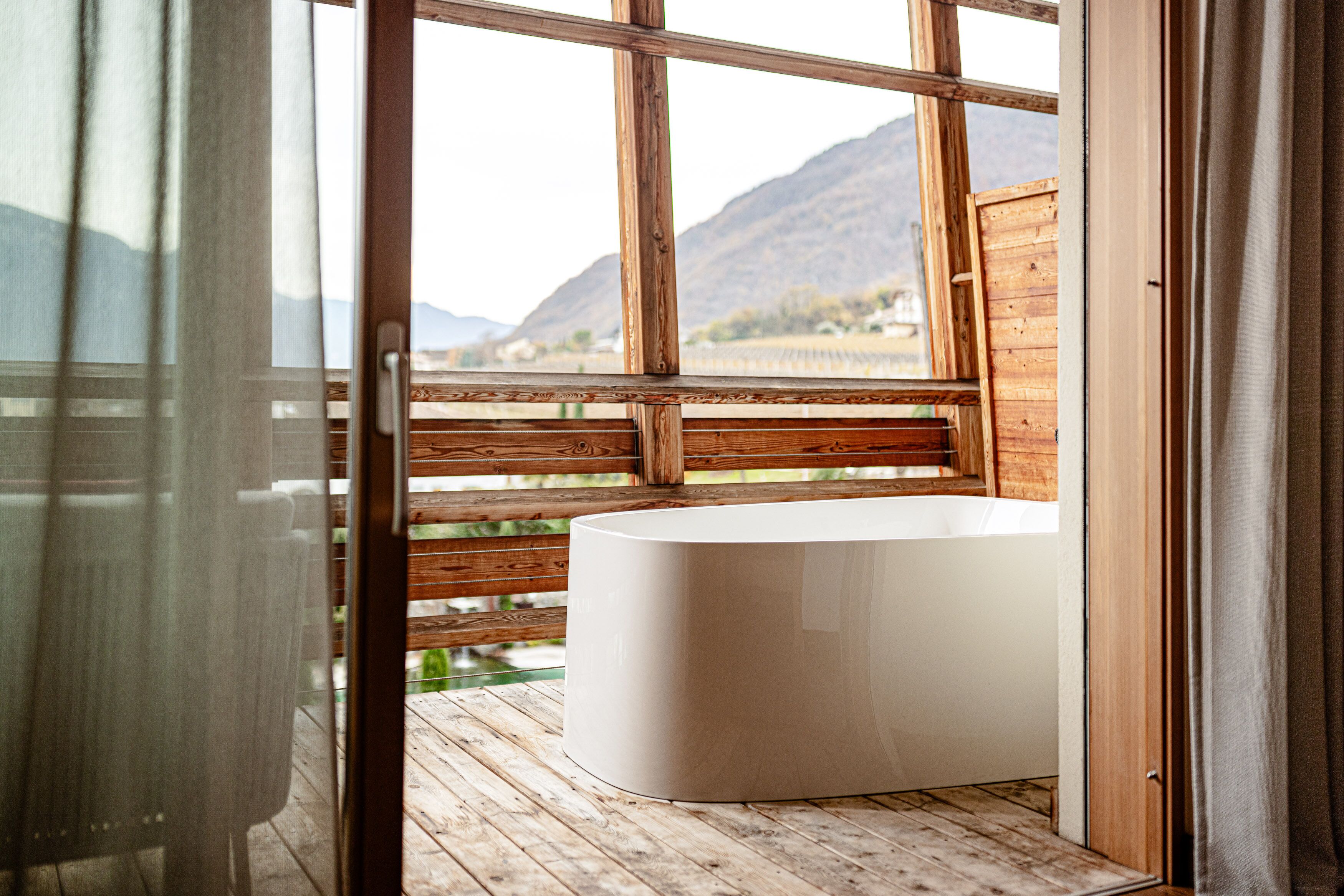 A wooden deck with a white bathtub, wooden railings, and a view of mountains.