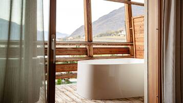 A wooden deck with a white bathtub, wooden railings, and a view of mountains.