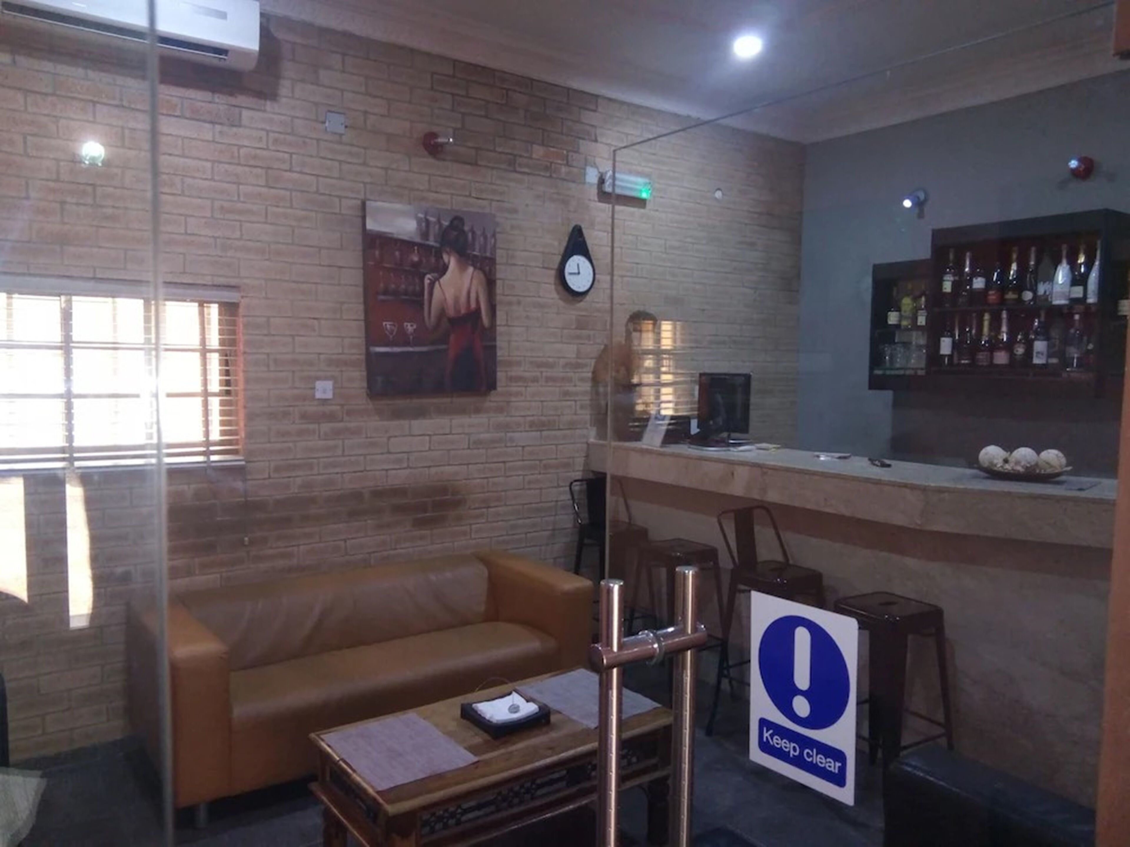 A hotel lobby with a brick wall, a sofa, a coffee table, a sign indicating a clear area, a clock, and a bar with bottles.