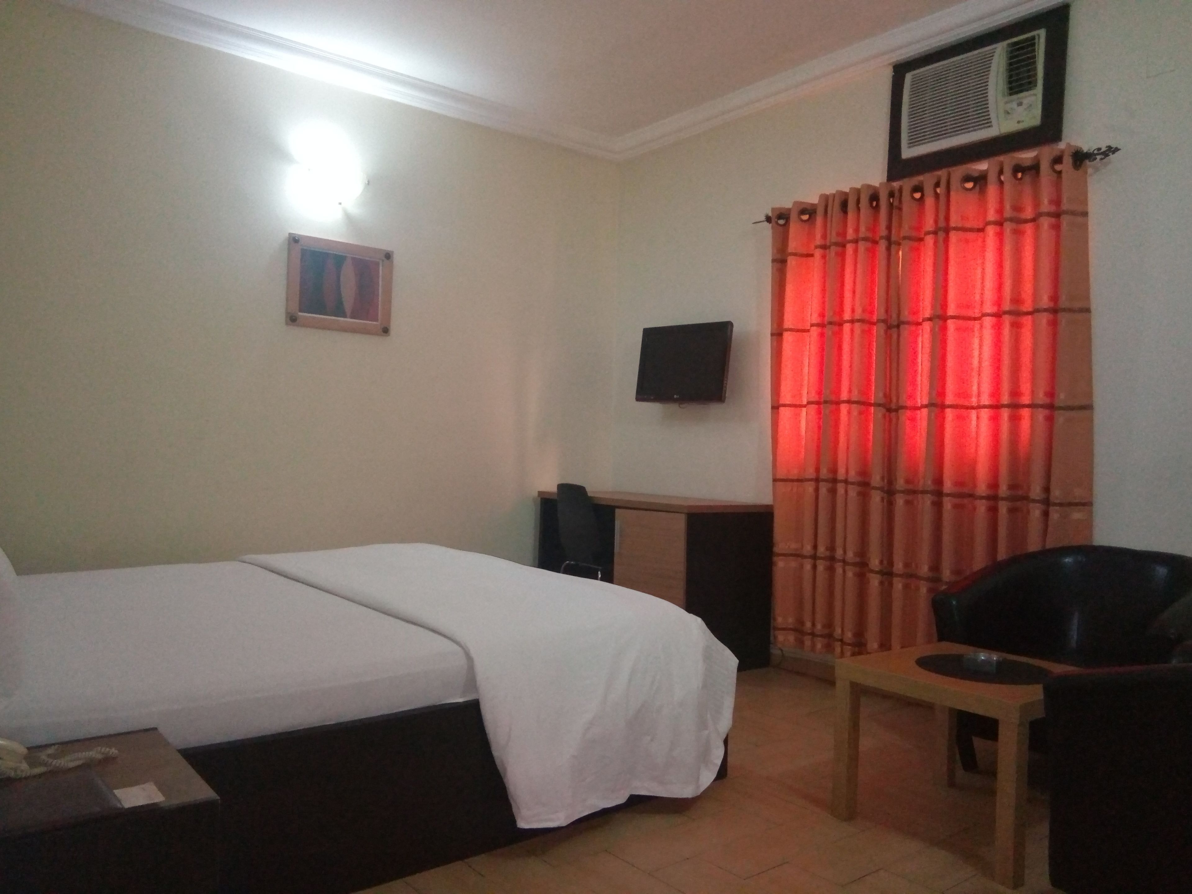 Habitación de hotel con cama, escritorio, silla, televisor y ventana con cortinas rojas.
